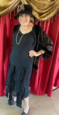 A guest in full 1920s flapper costume — black fringed dress, pearls, and period hat — before the curtain