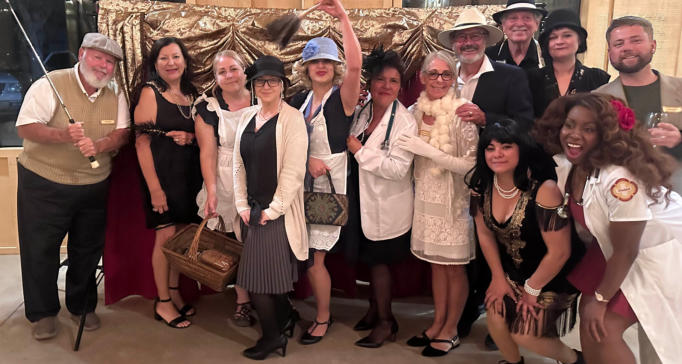 The full cast of guests in 1920s costume at a Murder Mystery party, gathered before the curtain